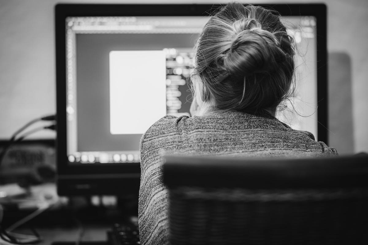 Femme assise devant un écran d'ordinateur, cheveux en chignon