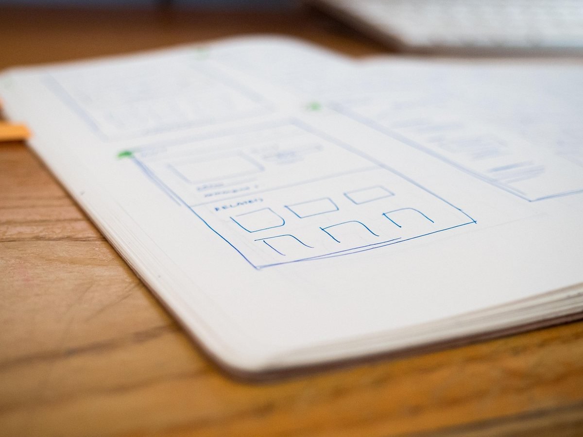 Un cahier ouvert sur une table en bois contenant des esquisses de wireframes Un cahier ouvert sur une table en bois contenant des esquisses de wireframes