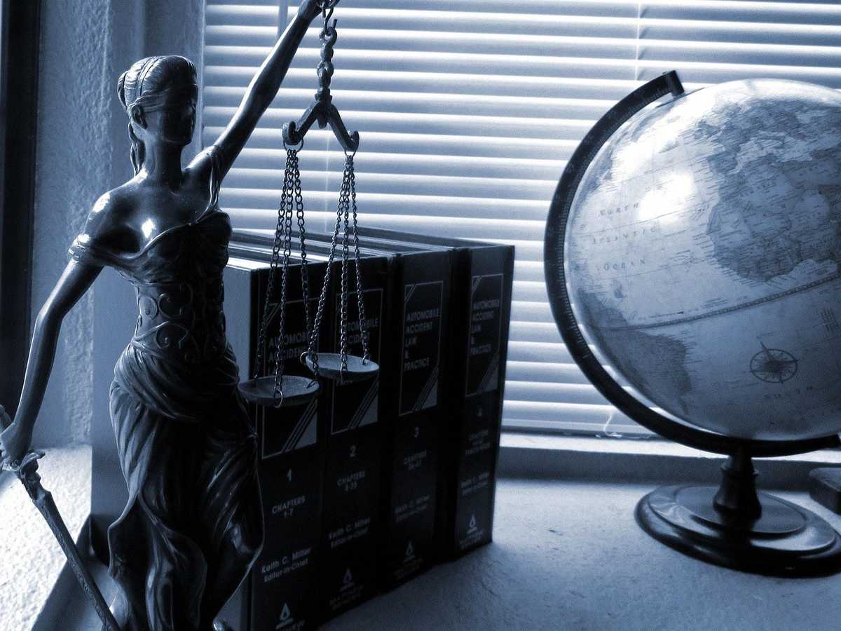Statue de justice tenant des balances, globe terrestre à droite, volets de fenêtre en arrière-plan