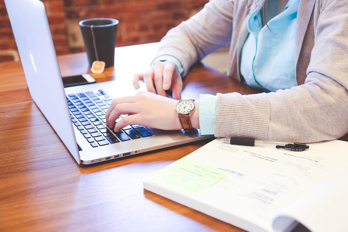 Une main avec montre tapote le clavier d'un ordinateur portable