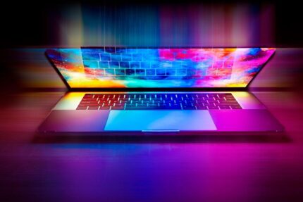 Laptop ouvert sur table, écran affiche un motif arc‑en‑ciel lumineux