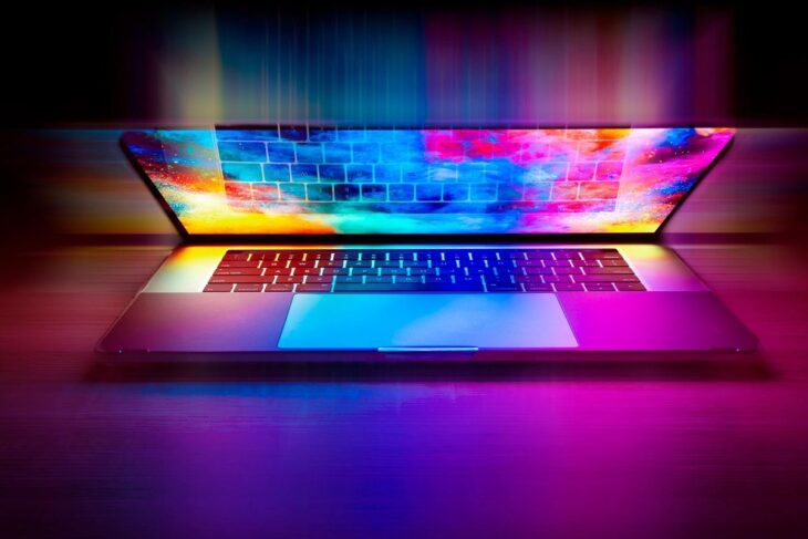 Laptop ouvert sur table, écran affiche un motif arc‑en‑ciel lumineux