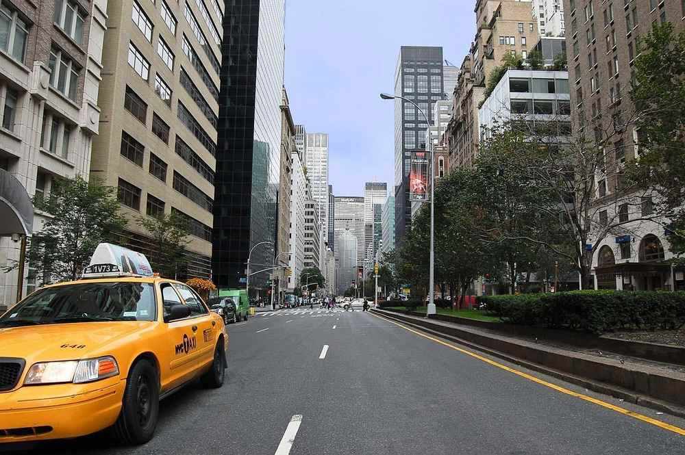 Rue de Manhattan avec taxi jaune stationné, immeubles de hauteur variée et arbres en arrière-plan Rue de Manhattan avec taxi jaune stationné, immeubles de hauteur variée et arbres en arrière-plan