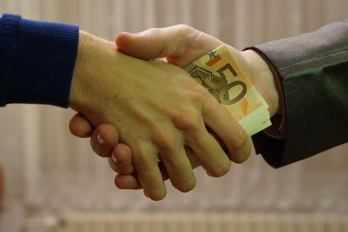 Homme en costume et homme en pull serrant la main avec des billets de 50 euros Homme en costume et homme en pull serrant la main avec des billets de 50 euros