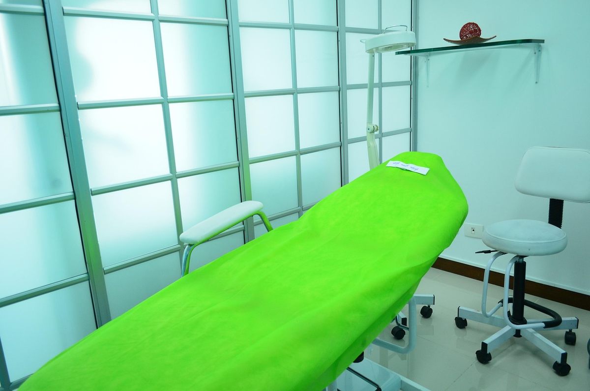 Une salle médicale avec lit vert, chaise roulante, lampe et étagère