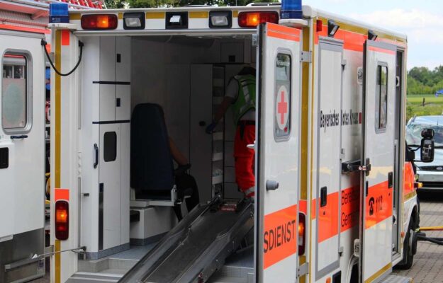 Ambulance avec porte ouverte, rampe déployée, personnel en tenue orange à l'intérieur