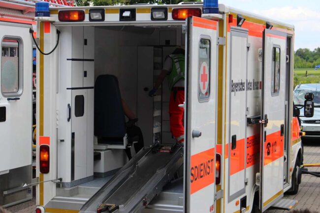 Ambulance avec porte ouverte, rampe déployée, personnel en tenue orange à l'intérieur